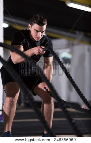 young fit athlete man working out in functional training gym doing  battle ropes exercise as part of cross fitness training