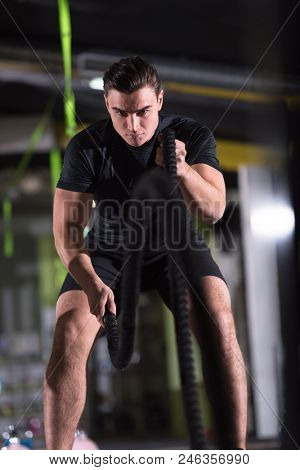 young fit athlete man working out in functional training gym doing  battle ropes exercise as part of cross fitness training