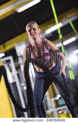 young fit athlete woman working out in functional training gym doing  battle ropes exercise as part of cross fitness training