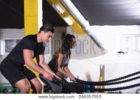 young fit sports couple working out in functional training gym doing  battle ropes cross fitness exercise
