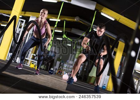 young fit sports couple working out in functional training gym doing  battle ropes cross fitness exercise