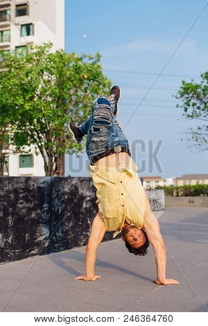 Young Handsome Man With Beard Dancing Breakdance On The Street. Man Stands On Hands.