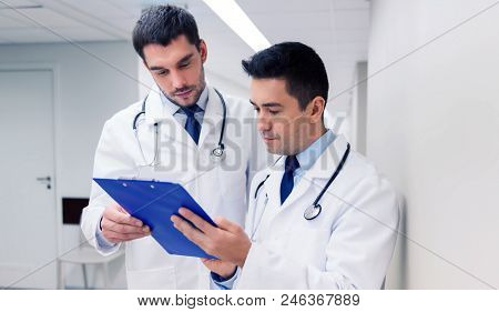medicine, healthcare and people concept - two male doctors with clipboard at hospital corridor
