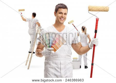 Painter holding a color swatch and a paint roller with two painters painting behind him isolated on white background