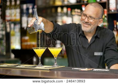 The Barman Pours An Orange Cocktail Into A Glass Beaker. The Bartender Pours The Cooked Ingredients 