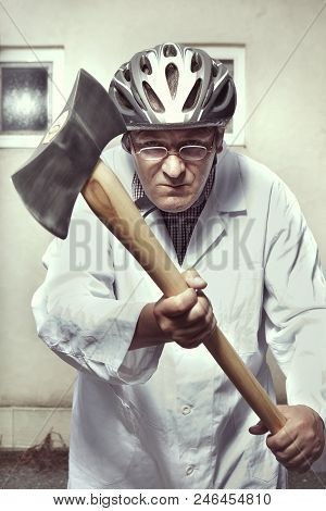 Older Paramedic Freak Man In Medical Coat And Protective Helmet Defending Itself With Double Axe