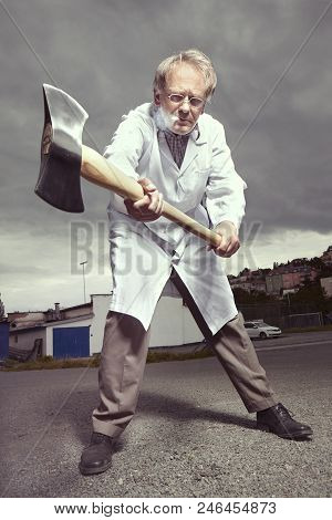 Older Paramedic Freak Man In Medical Coat And Protective Helmet Threating With Double Axe