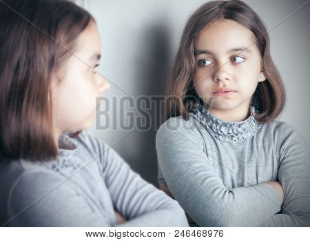 A Teenage Girl In A Gray Jacket Looks At Her Reflection In The Mirror.