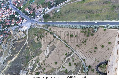 An Asphalt Road Leads To The Village Through A Brown Valley And Fields Between The Mountains, A View