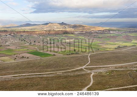 The Country Road Leads To The Village Through A Brown Valley And Fields Between The Mountains, A Vie