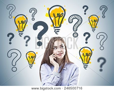 Dreamy Young Businesswoman Wearing A Blue Shirt Is Standing Near A Gray Wall With Many Question Mark