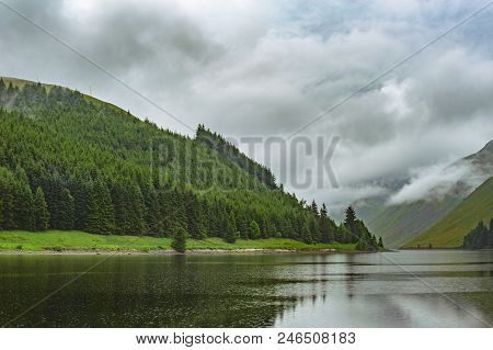 View Of A Beautlful Lake Talla In Scottish Borders With Green Hills Covered By Thick Rainy Clouds.