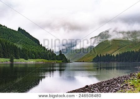 View Of A Beautlful Lake Talla In Scottish Borders With Green Hills Covered By Thick Rainy Clouds.