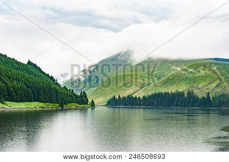 View Of A Beautlful Lake Talla In Scottish Borders With Green Hills Covered By Thick Rainy Clouds.