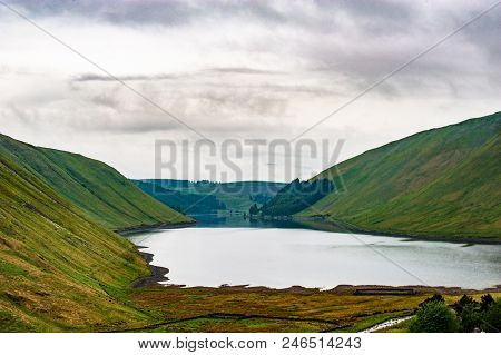 View Of A Beautlful Lake Talla In Scottish Borders With Green Hills Covered By Thick Rainy Clouds.