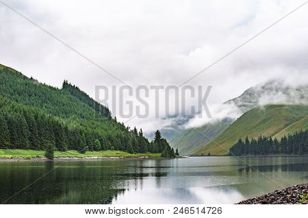 View Of A Beautlful Lake Talla In Scottish Borders With Green Hills Covered By Thick Rainy Clouds.