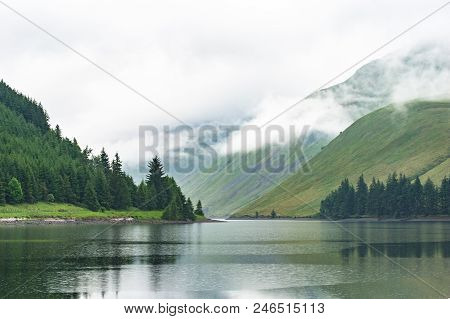 View Of A Beautlful Lake Talla In Scottish Borders With Green Hills Covered By Thick Rainy Clouds.