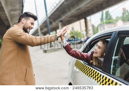 Happy Young Couple Giving High Five Each Other, Girl Sitting In Cab And Man Standing On Street