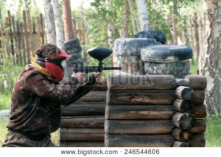 Playing In Paintball. A Girl Or A Guy In A Face Mask And Camouflage Uniform With A Weapon In Their H