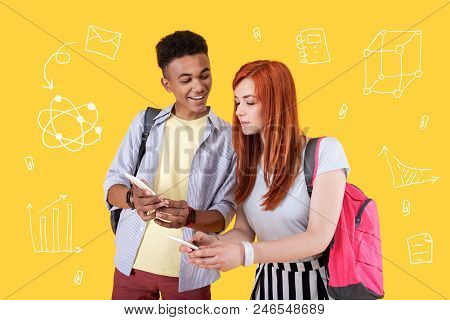 Sharing Phone Numbers. Cheerful Student Smiling While His Careful Fellow Student Holding A Modern Sm