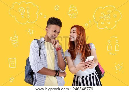 Funny Message. Cheerful Pretty Student Smiling And Showing A Funny Message To Her Serious Fellow Stu