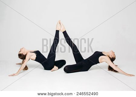 Two Athletics Girls Posing At White Studio, Leaning By Legs Each Other, Lying On Floor In Pose, Look