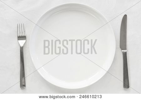 Empty white plate on brocade tablecloth with knife and fork.  Top view.