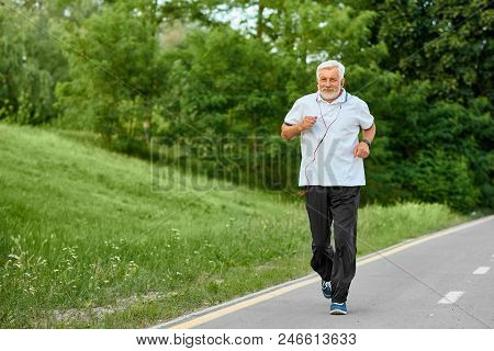 Fit Old Man Running On Racetrack In Green Park. Outdoors Sport, Trainings. Wearing Classic White Pol