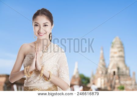 Thai Woman In Thai Dress Costume Traditional In A Welcome Pose, Hello Sawadee With Temple Background