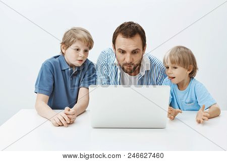 Father Watching Cartoons With Sons. Portrait Of Enterteined Attractive Father With Young Boys Sittin
