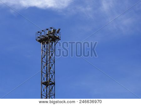 Steel Tower With Spotlights For Lighting The Railway Station Against A Blue Sky With Small White Clo