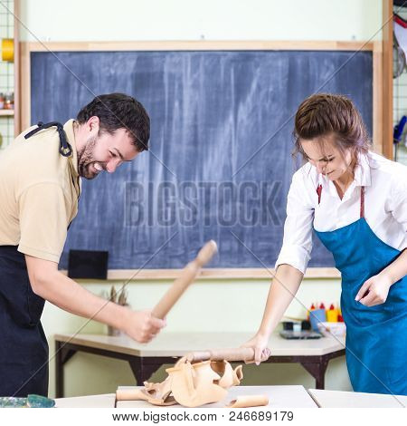 Two Caucasian Ceramists Squarrel And Crashing Clay Bowl On Table In Front With Rolling Pins. Negativ