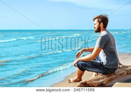 A Young Man With A Beard Sitting On The Beach And Looking At Dahl