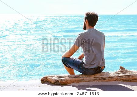 A Young Man With A Beard Sitting On The Beach And Looking At Dahl