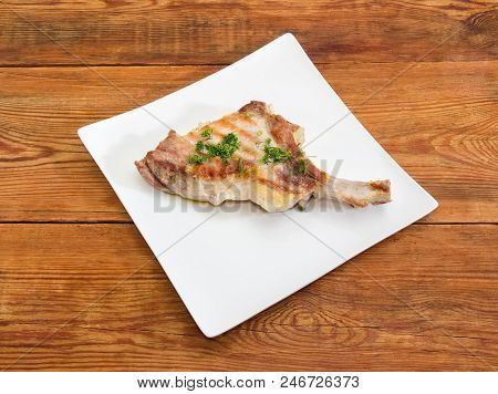 Grilled Pork Loin Chop With Partly Frenched Rib And Sprinkled With Chopped Dill On White Square Dish