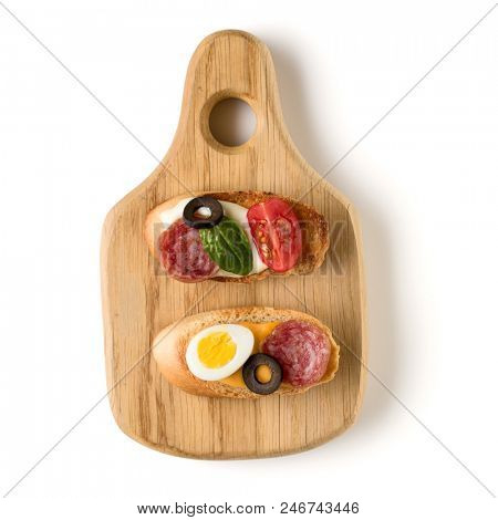Open faced sandwich canape or crostini on a wooden serving board isolated on white background closeup. Top view.