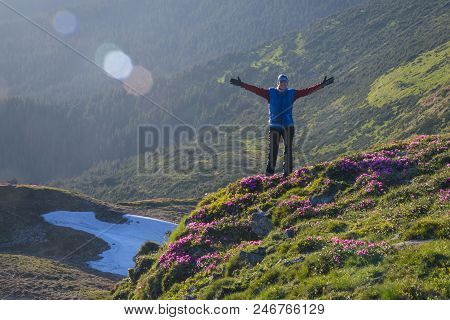 Happy Woman With Outstretched Hands On Blossom Mountain Slope. Dark Covered With Forest Mountains In