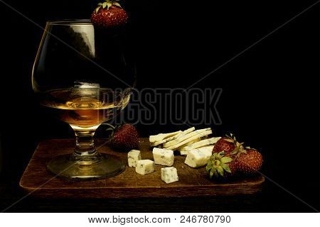Still Life With Cognac And French Blue Cheese On A Wooden Board. Glass With Cognac, Cheese, Strawber