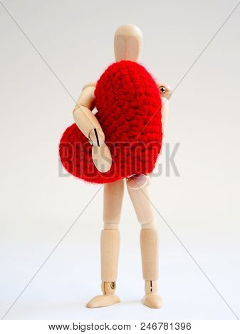 Wooden Puppet Standing And Holding A Red Heart On The White Screen Background. Wooden Puppet Holding