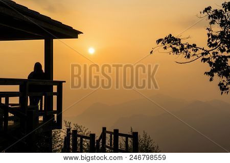 The Concept Of Travel. Silhouette Of A Girl Standing On The Porch Of A Wooden House With A Roof And 