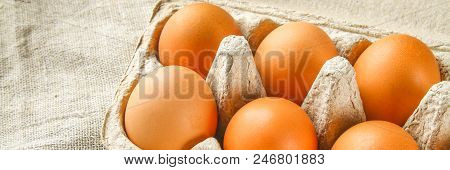 Raw Brown Chicken Eggs In A Cardboard Tray With Cells On Sacking On A White Wooden Table. Ingredient