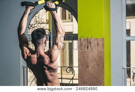 Sportsman, Athlete, Muscular Macho Does Exercise With Trx Loops, Window On Background. Sport And Gym