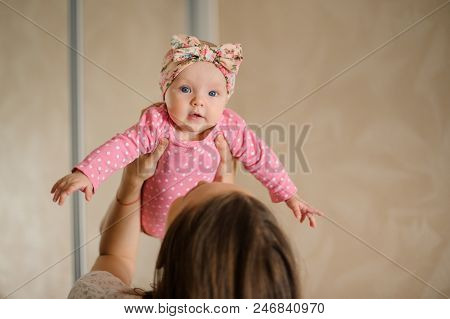 Mother Holding Her Lovely Little Daughter In The Pink Romper Up In The Air In Their Cozy Domestic Ro