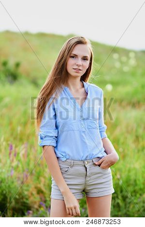 Happy Smiling Young Girl In Blue Shirt And Shorts In The Field