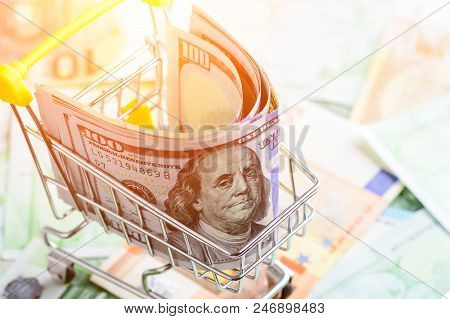One Hundred Dollar Bills In The Shopping Cart In Rays Of The Sun. Concept Of Necessary Expenditure A