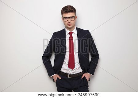 portrait of relaxed young businessman standing with hands in pockets on light gey background