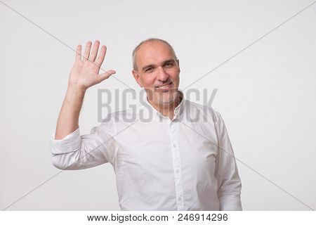 Handsome Attractive European Man Waiving Hand In Hello Gesture While Smiling Cheerfully. He Is Happy
