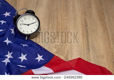 National Flag Of America And Black Alarm Clock On Old Wooden Background