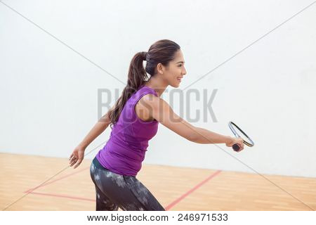 Side view of a young squash player holding the racket while standing with bent knees during game indoors on a professional court 