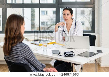 Dedicated doctor listening to her female patient while talking about symptoms during a private consultation in the office of a modern medical clinic